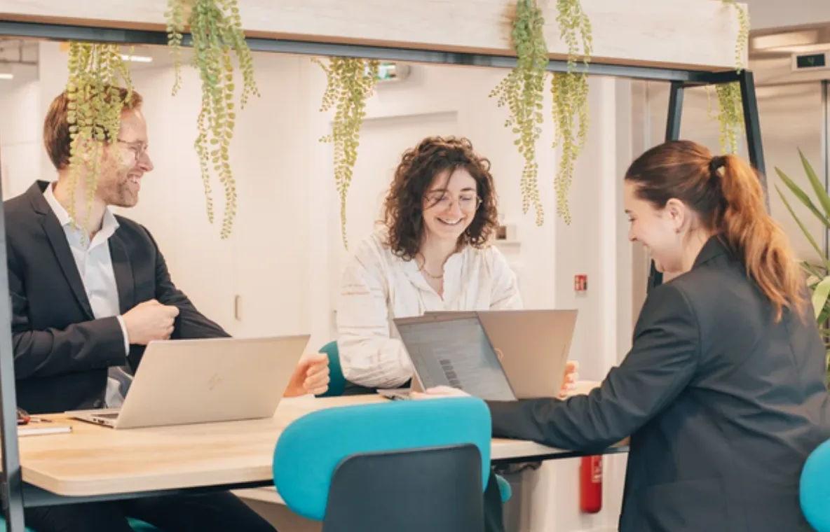 Trois collaborateurs échangent autour d’une table de travail végétalisée